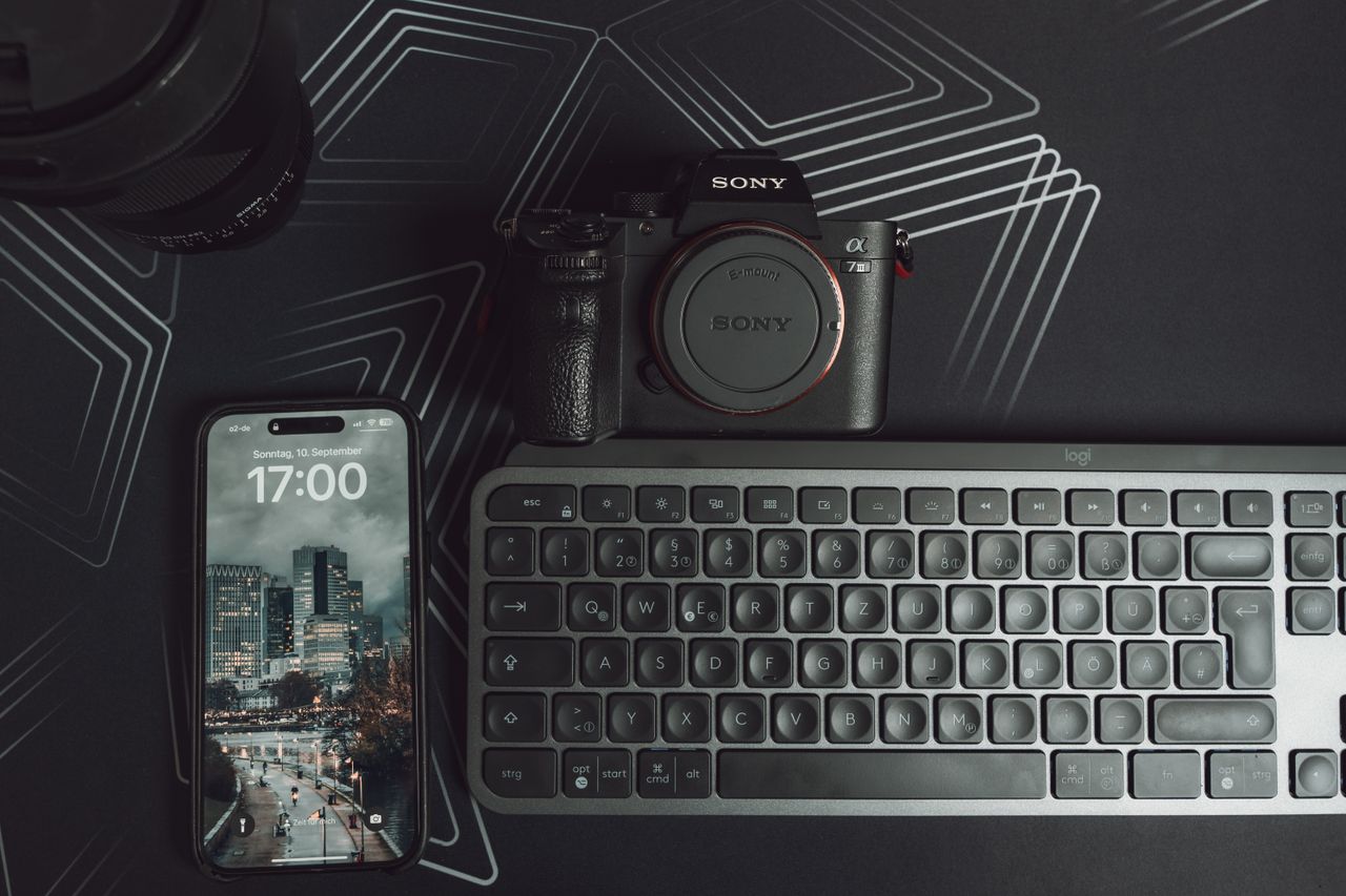 Elegant workspace setup featuring camera, smartphone, and keyboard on a geometric background.