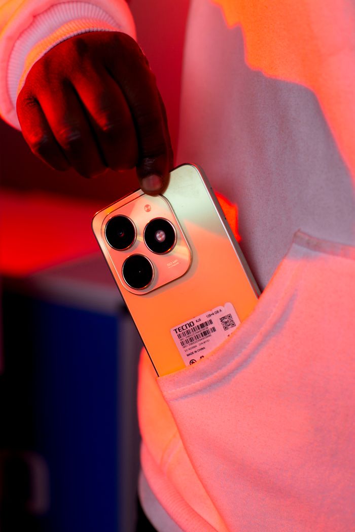 Close-up of a person placing a smartphone into a hoodie pocket with dramatic lighting.